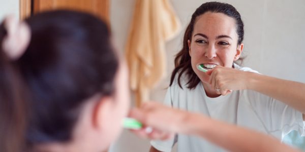 Smiling young woman brushing teeth in bathroom